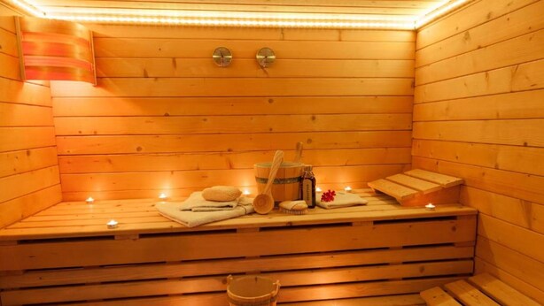 Una sauna de madera con bancos, un balde de madera y velas.