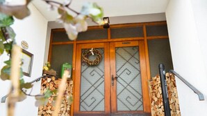 Una puerta de madera tradicional con un adorno de guirnalda, un letrero pequeño y una pila de leña a la izquierda.
