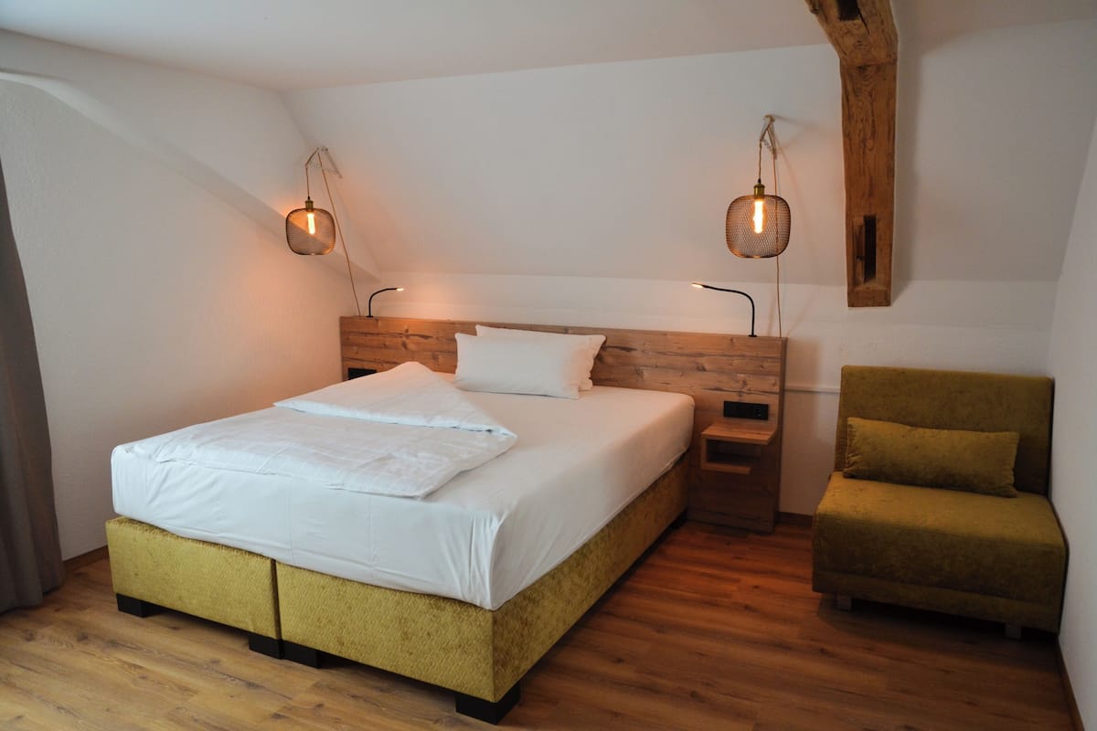 A bedroom with a wooden headboard, a bed with white bedding, two bedside tables, and a green armchair.
