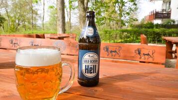 Un vaso de cerveza y una botella de cerveza Gold Ochsen Hell sobre una mesa de madera al aire libre.