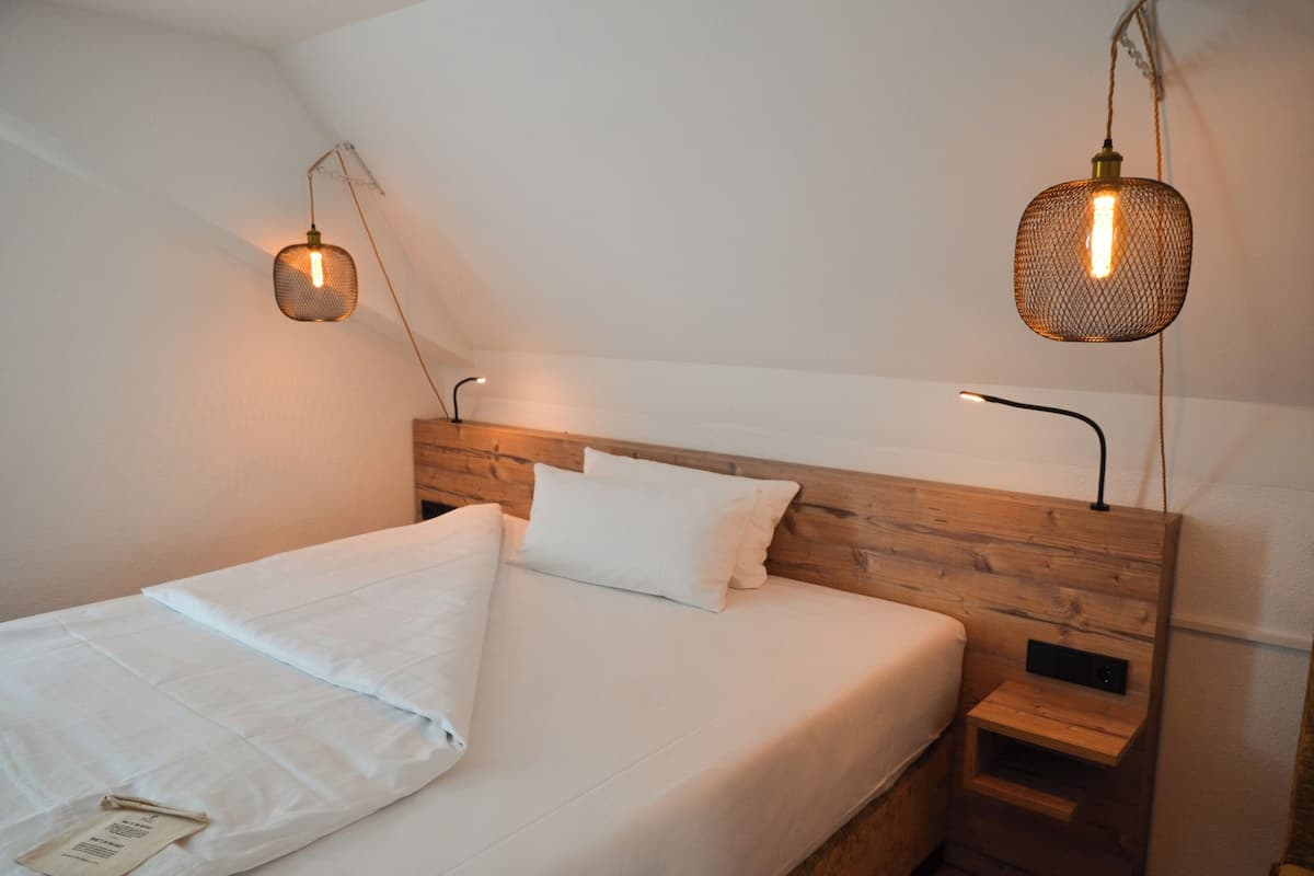 A neatly made bed with white linens, a wooden headboard, and a small bedside table with a lamp.