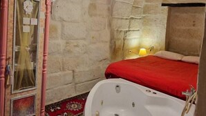 A rustic bathroom with a stone wall, wooden beams, a large bathtub, and a pink cabinet with glass doors. - King Solomon Palace  (Avanos)