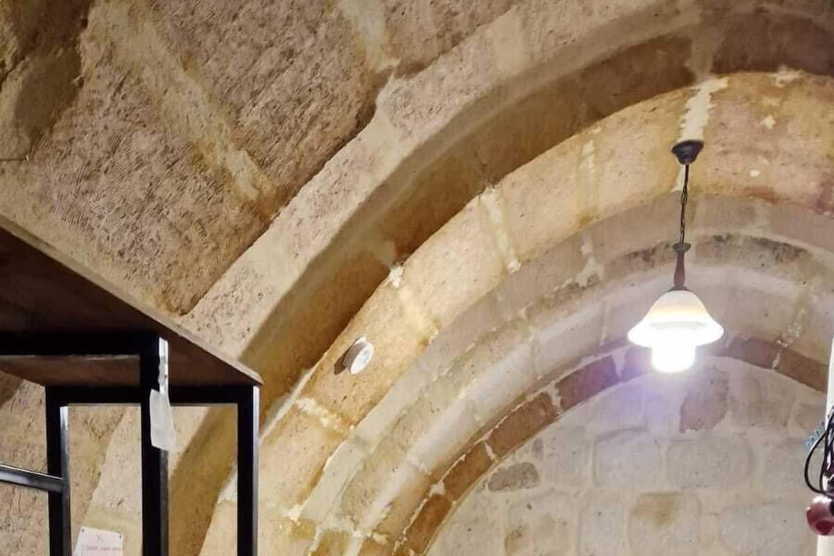 Una habitación con techo abovedado de piedra, cama con ropa de cama estampada, una estantería de madera y una alfombra con diseño.