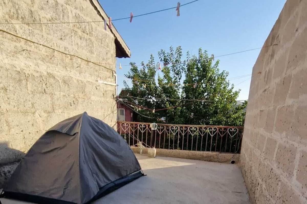 Una tienda de campaña montada en un patio con un muro de piedra y una verja de metal.