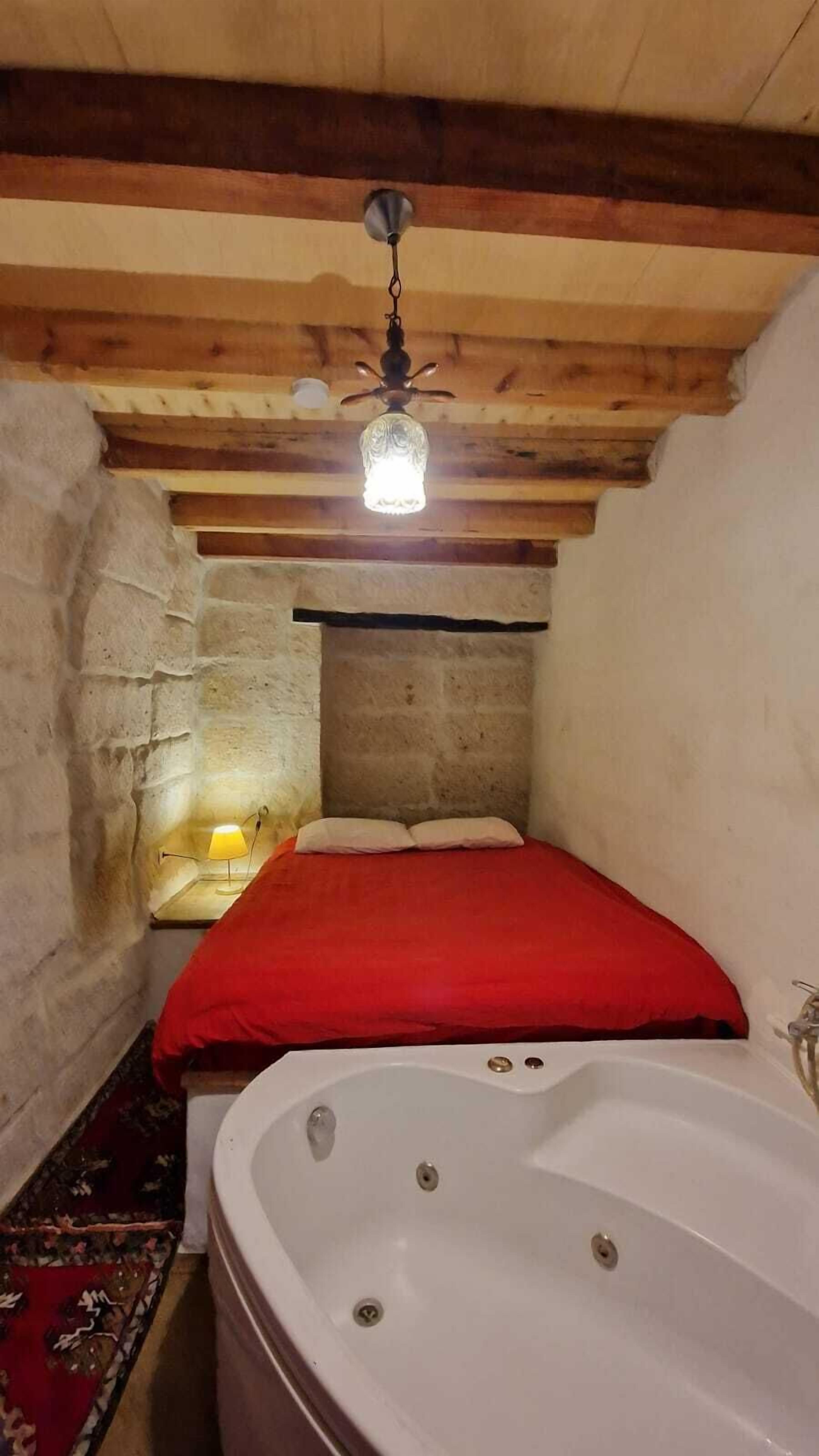 A small, cozy room with a single bed, a large bathtub, and a stone wall.