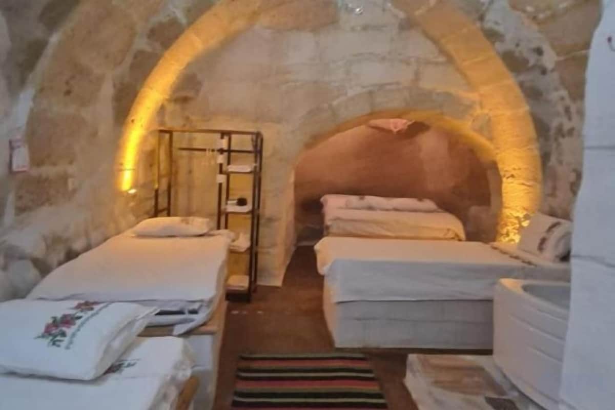 A stone-walled room with two beds, a bench, and a small table.