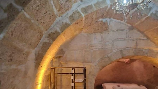 A stone-walled room with two beds, a chandelier, and a wooden shelf with towels. - King Solomon Palace  (Avanos)