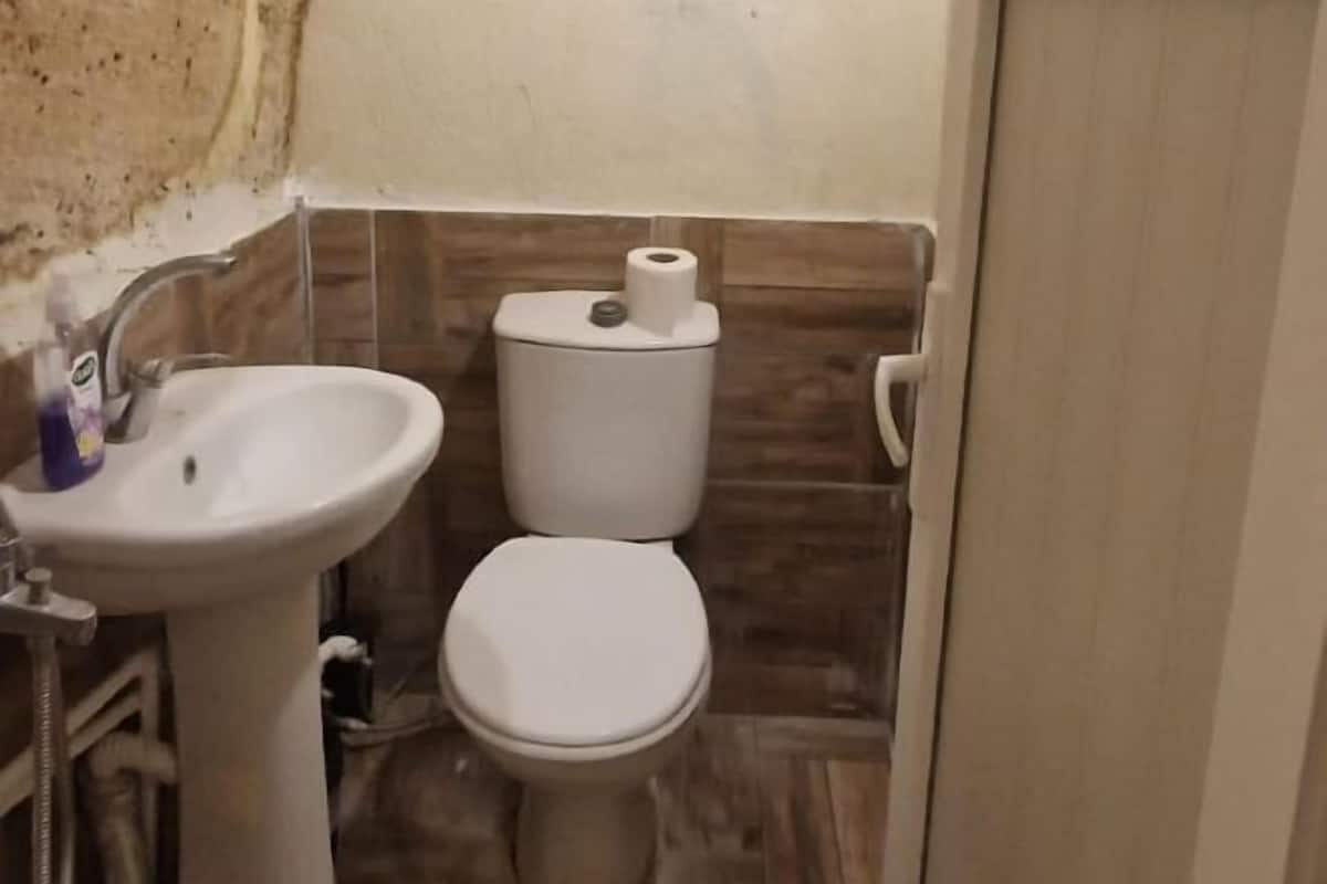Un baño con un lavamanos blanco, inodoro y un rollo de papel higiénico sobre el tanque.