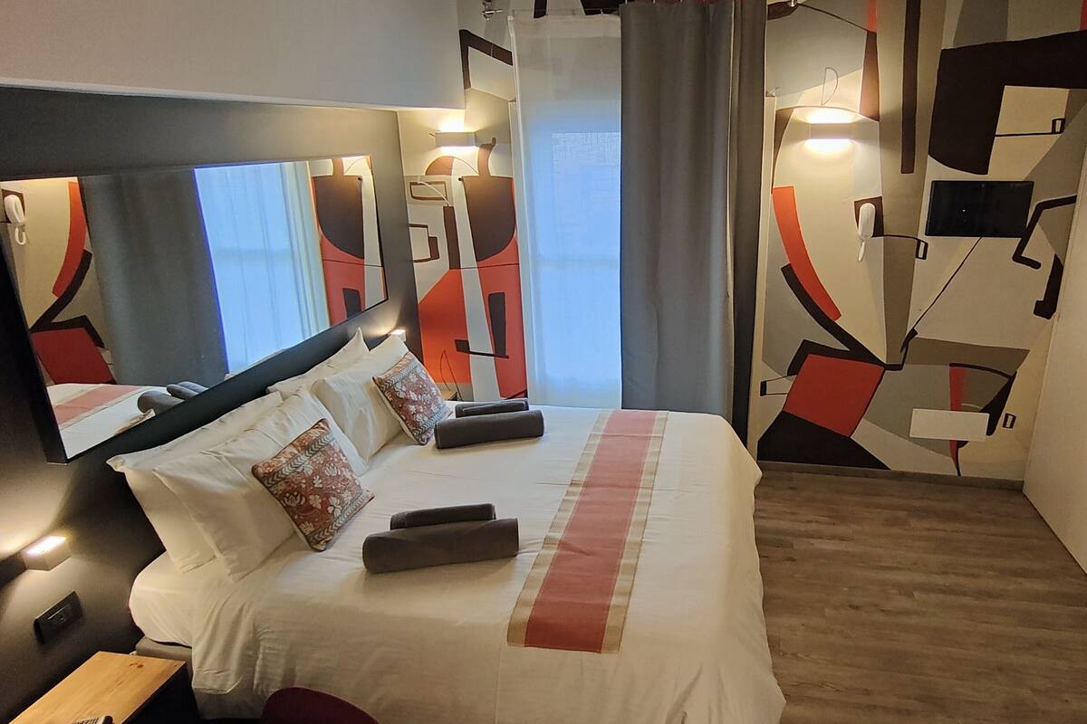 Quarto de hotel moderno com uma cama grande, um espelho, um guarda-roupa e uma mesa de cabeceira.