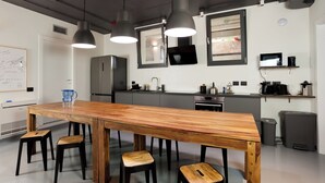 A modern kitchen with a wooden dining table, black stools, pendant lights, a refrigerator, a microwave, and a sink. - ANNAMA Coliving (Brescia)