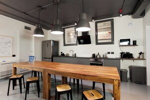 Una cocina moderna con una mesa de comedor de madera, taburetes negros, luces colgantes, un refrigerador, un microondas y un lavamanos.