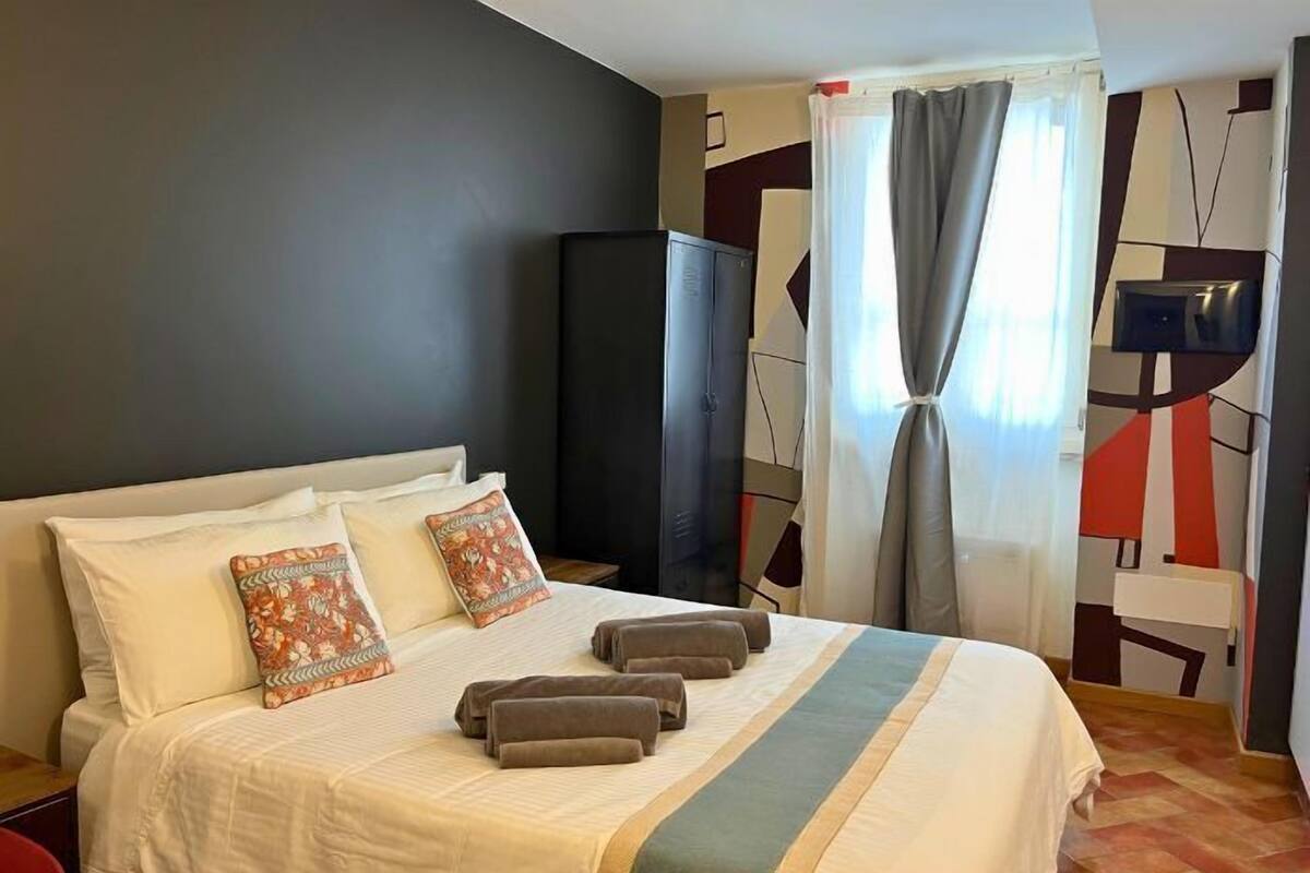 Quarto de hotel com cama, almofadas, televisão e guarda-roupa.