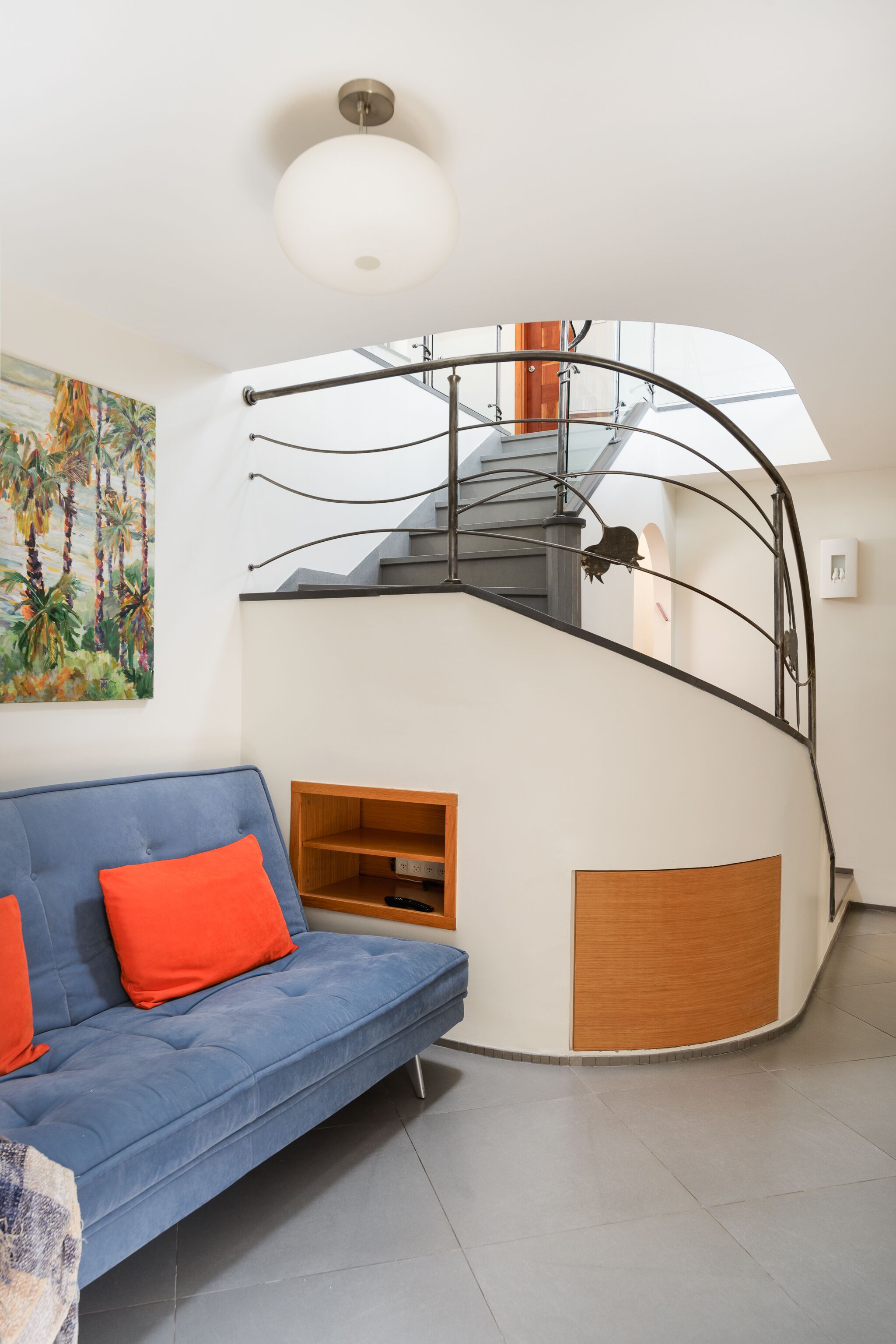 A modern living room with a blue sofa, a wooden cabinet, and a curved staircase with a metal railing.