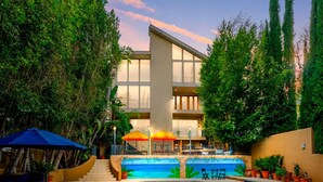 Ein modernes Hotel mit Swimmingpool, Sitzgelegenheiten im Freien und üppiger Bepflanzung.