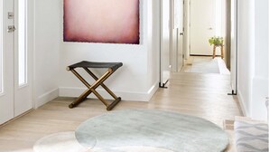 Um corredor com design de interiores moderno, apresentando uma grande pintura abstrata na parede, uma cadeira preta dobrável e um tapete multicolorido no chão.