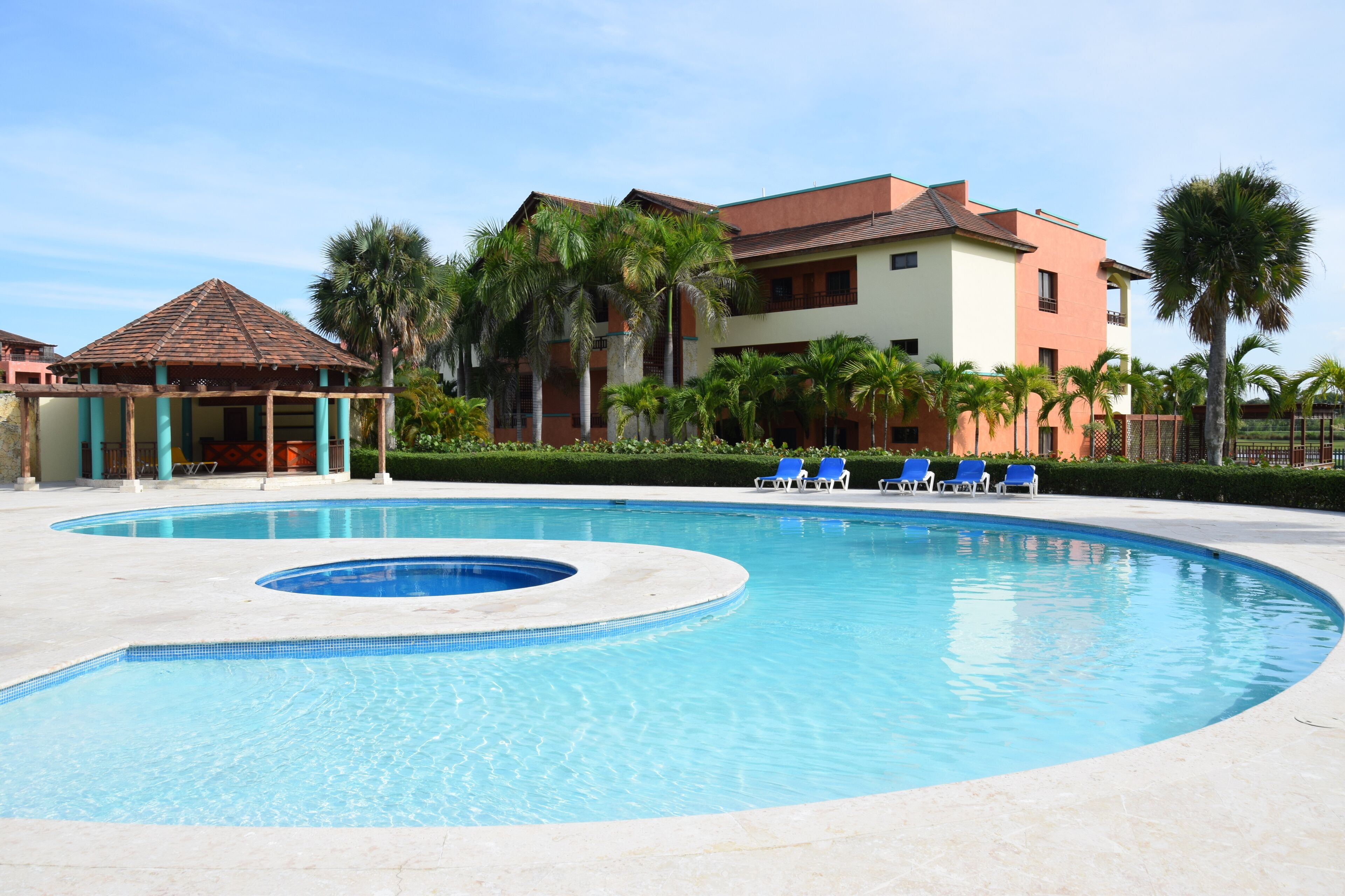 Piscina com água azul, rodeada por espreguiçadeiras e palmeiras.