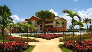 A hotel with a central courtyard, palm trees, and red flowers. - Magic Arena Blanca Beach Suite (Punta Cana)