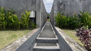 A pathway leading to a building with a modern architectural design, flanked by lush greenery and concrete walls. - Belvilla Darshana Bali Zoo (Batubulan)