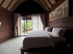 A bedroom with a large bed, wooden walls, a sloped ceiling, and a view of the outdoors. - Belvilla Darshana Bali Zoo (Penatih)