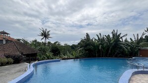 A swimming pool with tiled edges, surrounded by lush greenery and a thatched-roof structure. - Belvilla Darshana Bali Zoo (Batubulan)