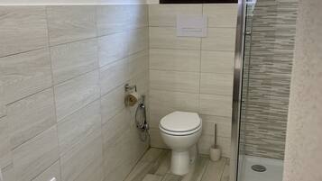 A bathroom with a toilet, a shower, and a window.