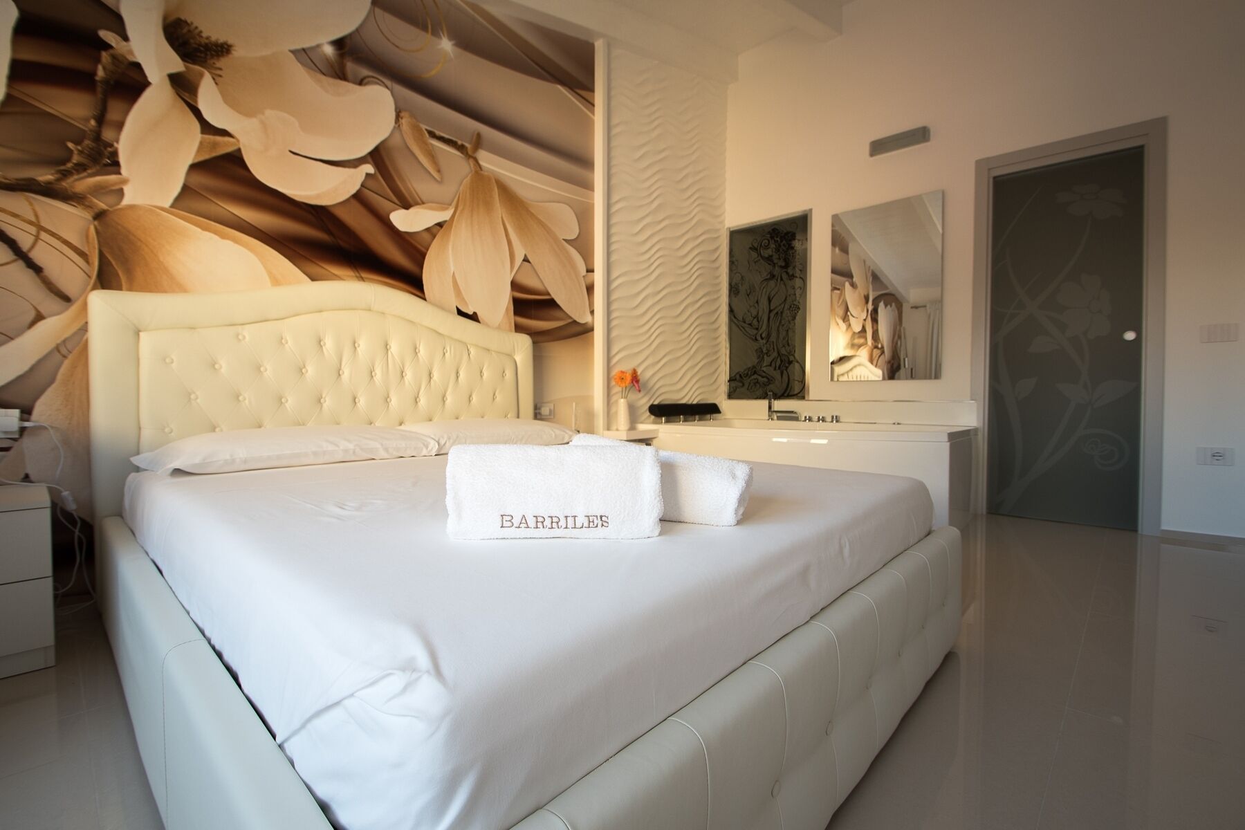 Un dormitorio moderno con un cabecero capitonado, una cama grande, un tocador con espejo y una puerta con estampado floral.