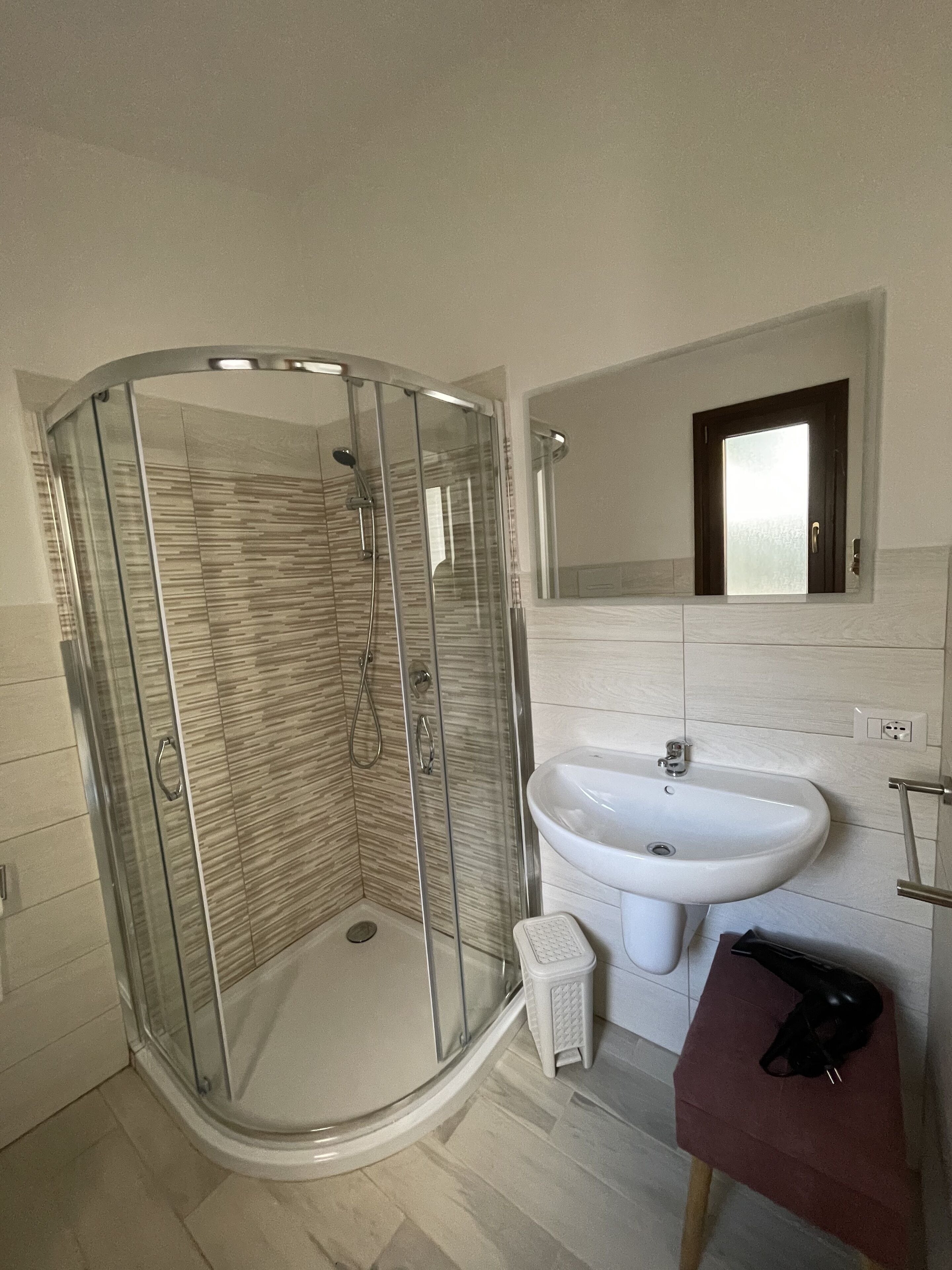A modern bathroom with a glass-enclosed shower, a white sink, and a small vanity.