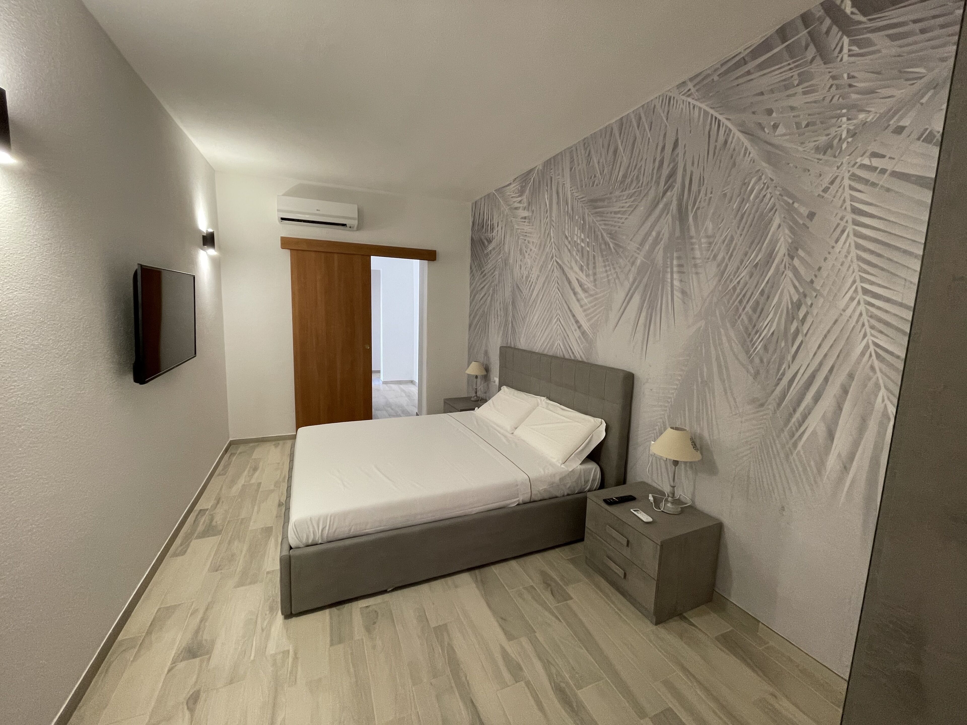A modern bedroom with a bed, bedside table, lamp, and a wall-mounted air conditioner.