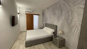 A modern bedroom with a bed, bedside table, lamp, and a wall-mounted air conditioner.
