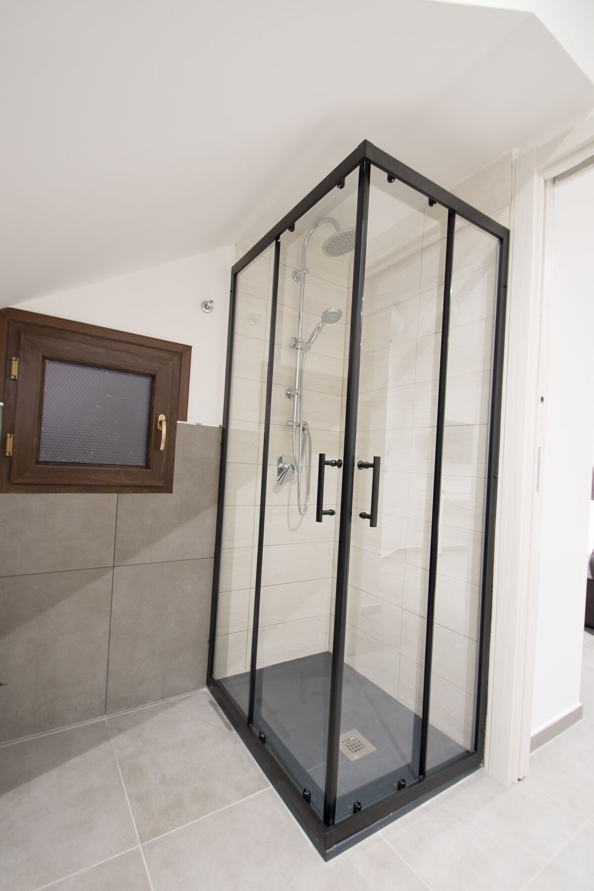 Zona de ducha con cerramiento de vidrio, ducha con cabezal, ducha de mano y panel de control.