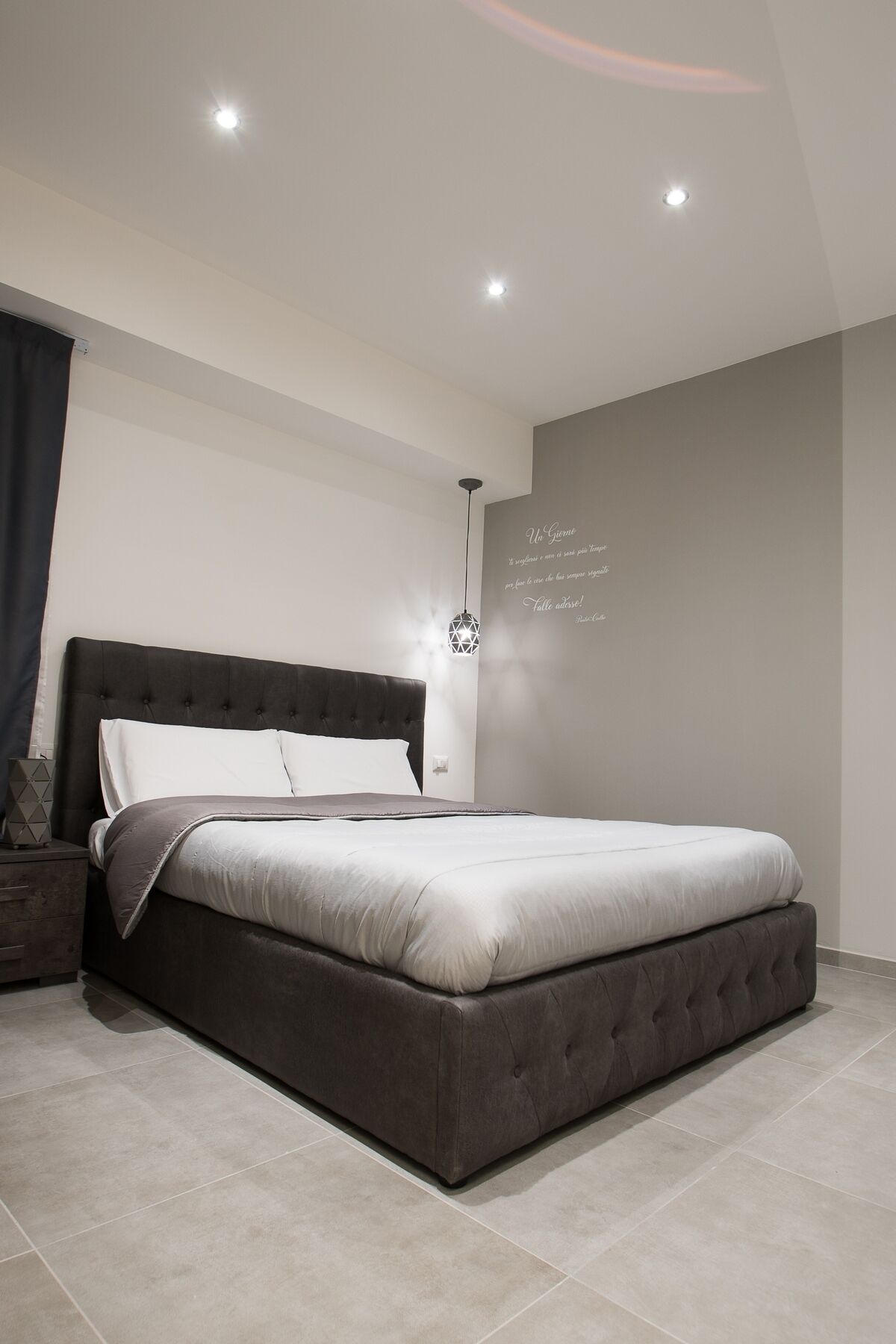 Un dormitorio moderno con una cama grande, una mesita de noche y una lámpara de pared.