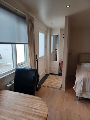 A hotel room with a wooden floor, a round table, a bed with a striped blanket, a window with curtains, and a mirror on the wall. - Nordurgata 43 (Akureyri)