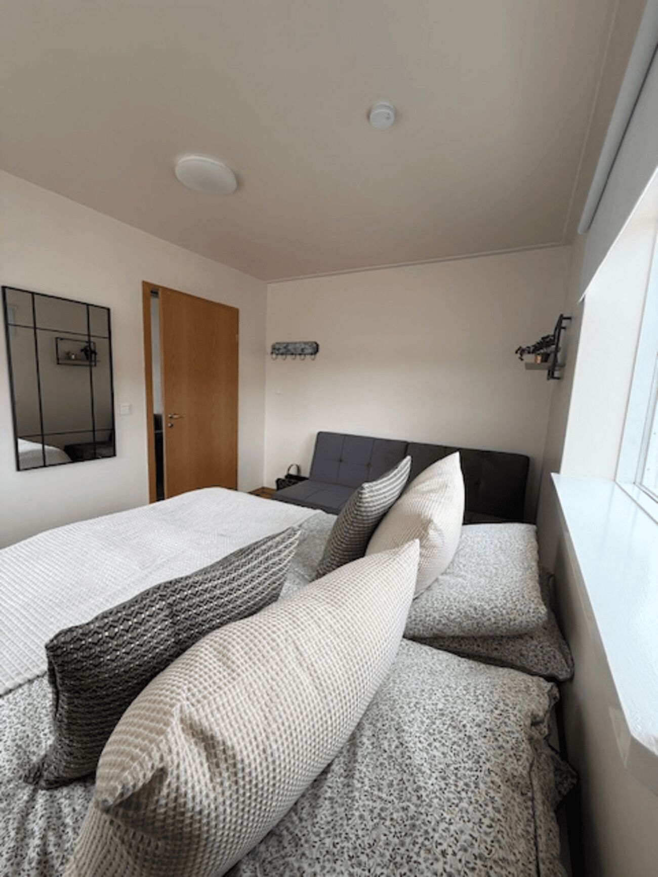 A bedroom with two beds, a wooden door, a mirror, and a window with a view.