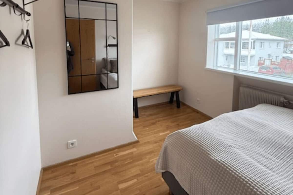 A bedroom with a bed, a bench, a mirror, and a window.