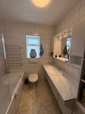 A modern bathroom with a bathtub, toilet, and sink. There is a window with a towel hanging outside, and a mirror above the sink. - Nordurgata 43 (Akureyri)