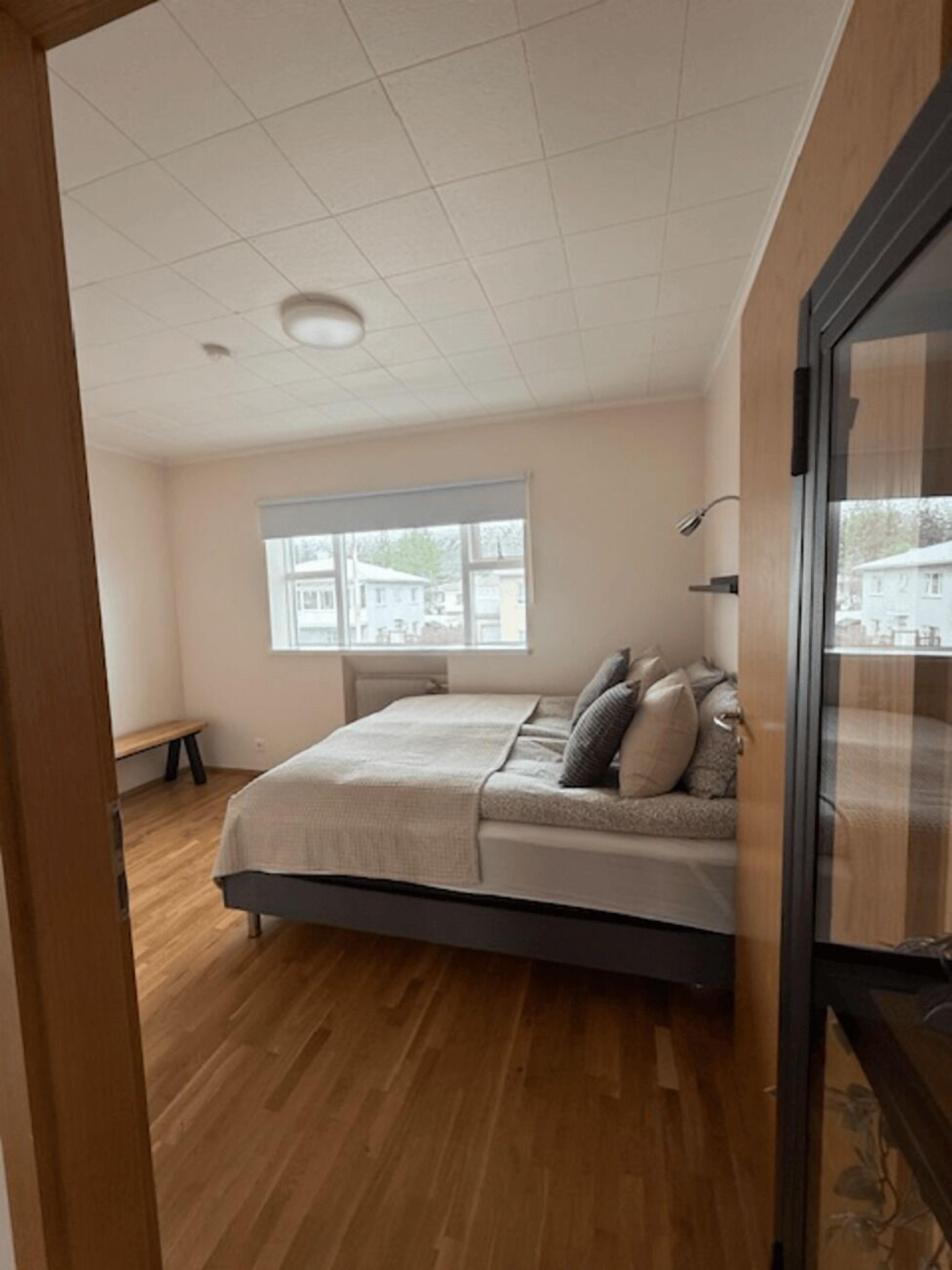 Ein Schlafzimmer mit Bett, Fenster, einer Bank und Blick auf Gebäude.