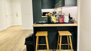 A modern kitchen with dark cabinets, a wooden countertop, and two stools. - Your London Escape Luxurious 1 Bedroom Apartment (Wembley)