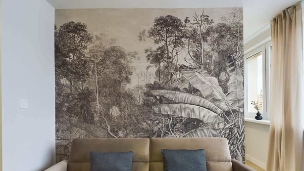 A living room with a beige sofa and a large wall mural depicting a forest scene. - Modern Studio with Workspace | Close to Metro (Warszawa)