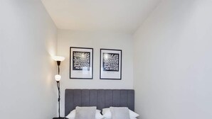 A bedroom with a bed, two pillows, a bedside table, a lamp, and two framed artworks on the wall. - Modern Studio with Workspace | Close to Metro (Warszawa)