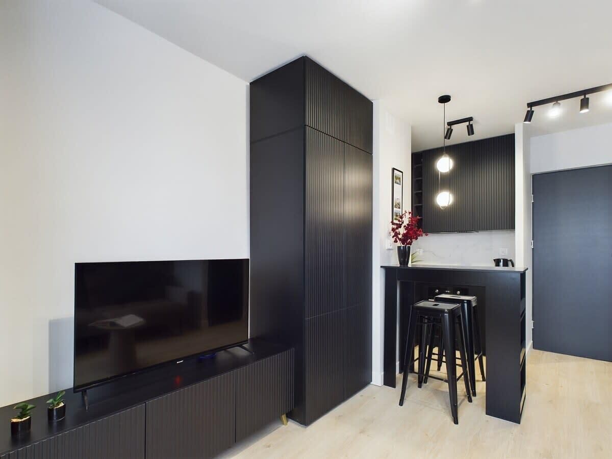 Una cocina moderna con televisor integrado, armarios oscuros y una pequeña zona de bar con taburetes.