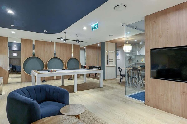 The modern recreation room, with wooden panels and subtle lighting, offers a variety of entertainment, from billiards to watching TV, creating a space ideal for relaxation and meetings.