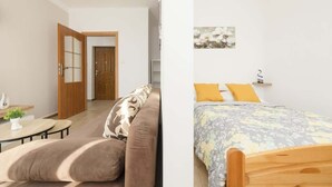 A room with a wooden bed, a sofa, a small table with a plant, and a door leading to another room.