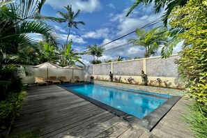 Une piscine dotée d’une terrasse en bois, entourée de palmiers et d’un mur de pierre.