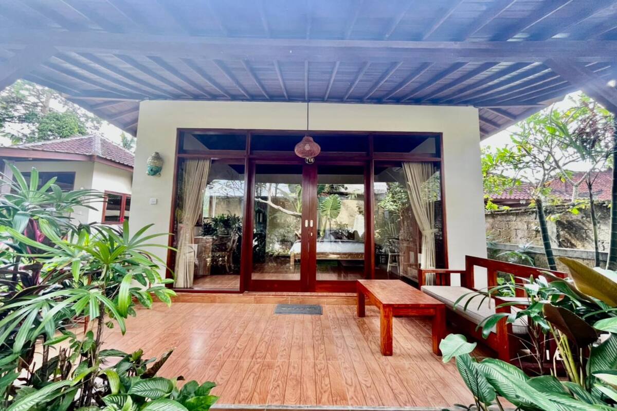 A covered patio with wooden flooring, a bench, and potted plants.