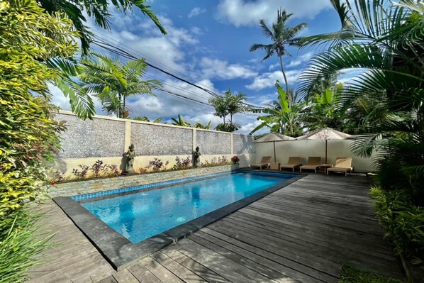 Une piscine rectangulaire dont les bords sont recouverts de carrelage, entourée d’une terrasse en bois.