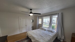 A bedroom with a bed, a ceiling fan, a window with curtains, and a rug.