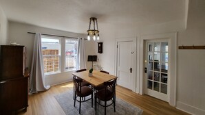 A dining area with a wooden table and chairs, a chandelier, a window with curtains, and a door with glass panels.