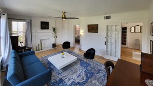 A living room with a white ceiling, a ceiling fan, a white fireplace, a blue sofa, a white coffee table, and a patterned rug.