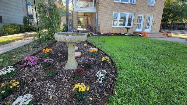 A two-story house with a front porch, a birdbath, and a well-maintained garden with various flowers.