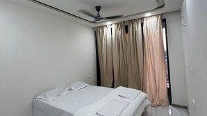 A bedroom with a single bed, a ceiling fan, and a window with curtains. - Ayarkar Farm Resort (Murud)